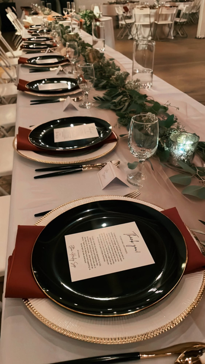 Black and gold place settings with terracotta napkins along a greenery runner